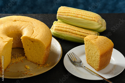Corn cake on a plate on a black base, ears of green corn on the table, blue background