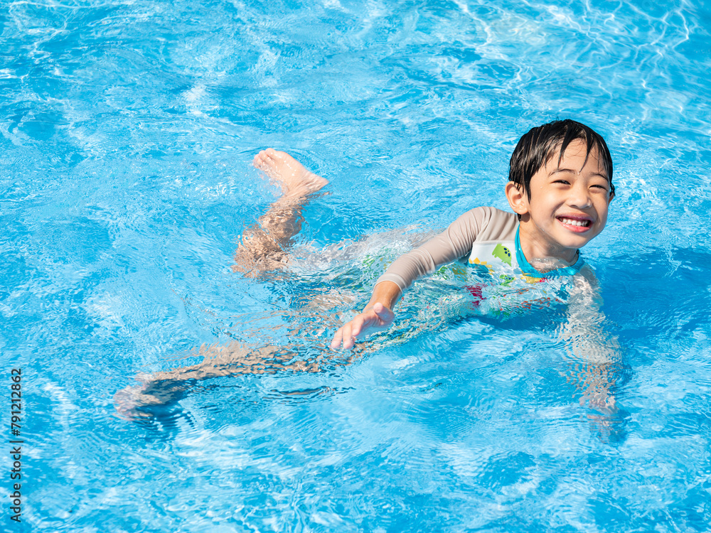 Happy Asian cute boy five years old is swimming and playing in the blue clear swimming pool. He is relaxing during his summer holidays.