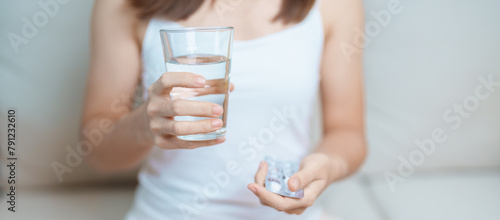 woman hand holding medicine painkiller pill and water glass on the sofa at home, taking for headaches, stomach ache, Diarrhea Pain from food poisoning, Endometriosis, Hysterectomy and Menstrual