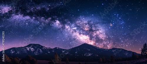 Scenic view of a dark night sky filled with shimmering stars and the Milky Way galaxy stretching above mountains in the background © LukaszDesign