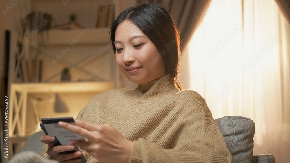 Bank app. Electronic money. Digital payment. Happy satisfied woman using credit card for mobile phone in home interior. Bank app. Electronic money. Digital payment. Happy satisfied woman using credit card for mobile phone in home interior.