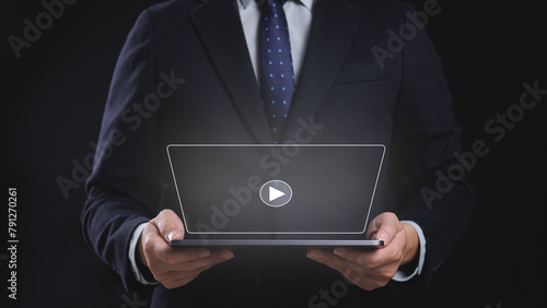 A man in a suit holding a tablet with a virtual screen display a play button on it. Concept of professionalism, focus and online video streaming and social media.