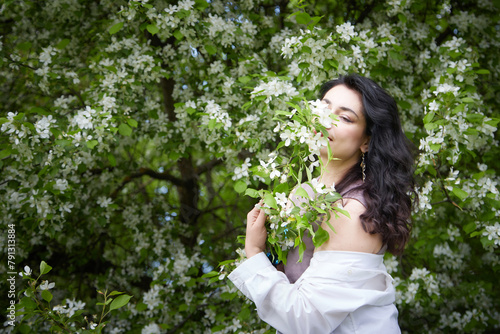 Joyous brunette woman near Blossoms of apple tree in a Spring Garden outdoors. Concept of face and body care. The scent of perfume and tenderness