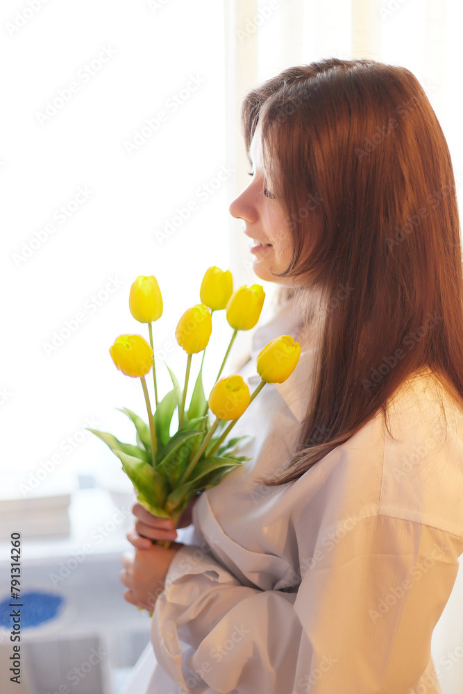 Beautiful sweet girl in nightgown in early morning with bouquet of delicate yellow tulips. Gift on International Women's Day on March 8th. Cosmetics, skin care, hair care. Perfume, natural fragrance