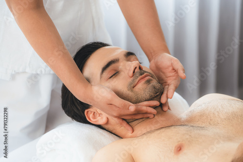 Caucasian man enjoying relaxing anti-stress head massage and pampering facial beauty skin recreation leisure in dayspa modern light ambient at luxury resort or hotel spa salon. Quiescent