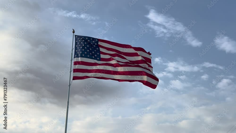 Large American Flag Blowing in the Wind against a sunny blue sky and white clouds in late afternoon Large American Flag Blowing in the Wind against a sunny blue sky and white clouds in late afternoon