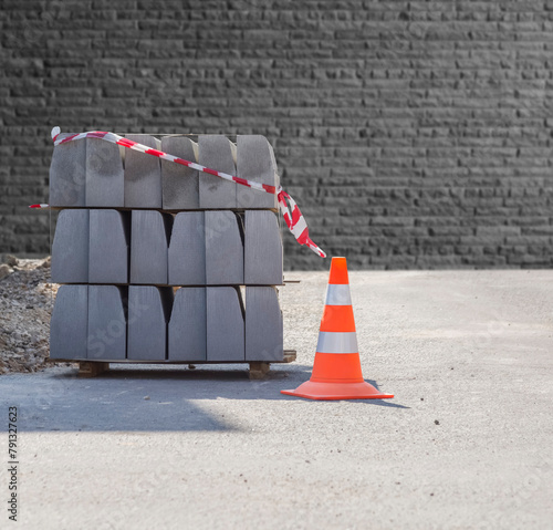 A traffic cone and a pallet with a curb stone on the background of a gray brick wall