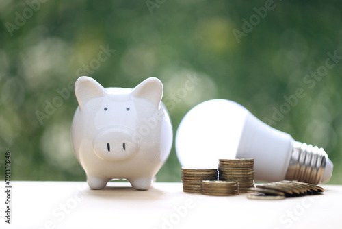 Piggy bank and stack of coins money with light bulb on natural green background,Saving money and energy saving concept