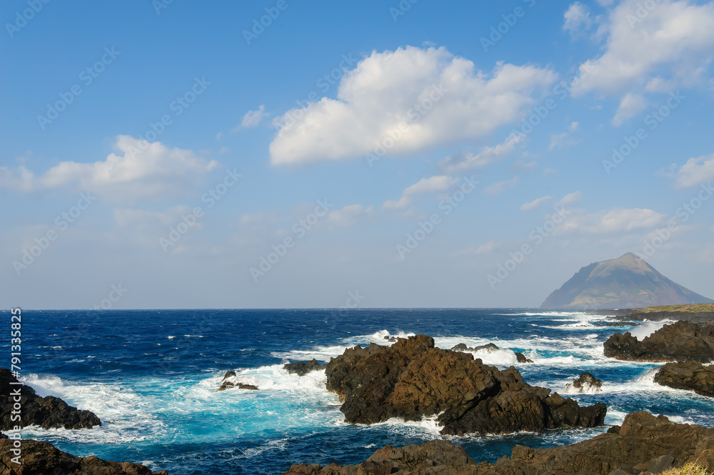 Fototapeta premium 太平洋の荒波を受ける島中央南岸の八重根港。 巨大な防波堤に守られた水域は有力なダイビングポイント。航路の終点、太平洋の大きな孤島、八丈島。 東京都伊豆諸島。 2020年撮影。Yaene Port on the south coast of the central island is subject to the rough waves of the Pacific Ocean. The w