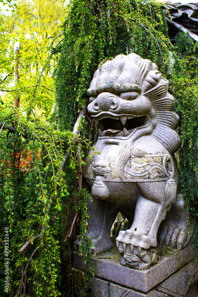 Guardian of the Garden: Stone Lion Statue Amidst Verdant Foliage