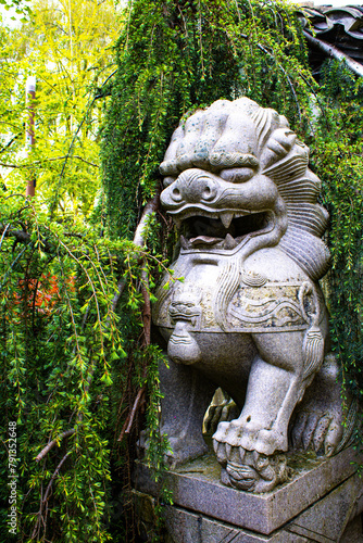 Guardian of the Garden: Stone Lion Statue Amidst Verdant Foliage © brettar