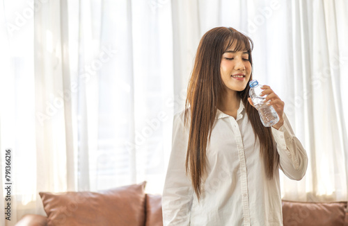 Portrait asian beauty body slim woman drinking water from a bottle while relax and feeling fresh   refresh drink  wellness  diet  healthcare  mineral at home.Healthy liquid lifestyle concept