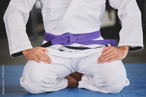 Martial arts, fitness and person kneeling in gym for training, uniform and professional fighting sport. Health, wellness and Brazilian jiu jitsu athlete in dojo with gi, respect and sitting on mat