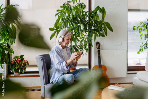 Older woman with headphones on head, listening music, relaxing at home. photo