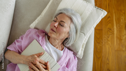 Top view of beautiful mature woman asleep with book. Weekend activity for older woman, relaxing at home.