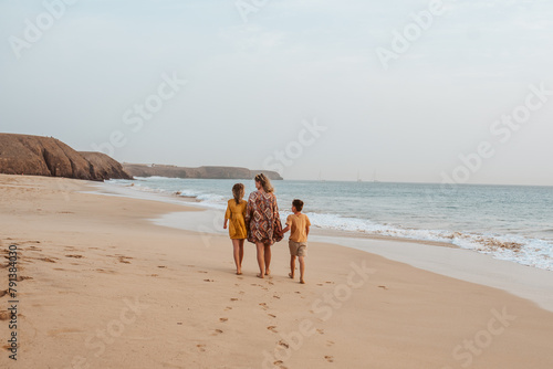 Mother with two kids on beach. Young family enjoying sandy beach in Canary Islands. Concept of beach summer vacation with kids.