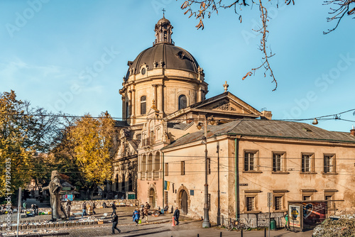 Lviv, Ukraine - November 2, 2023: Ivan Fedorov Statue in the middle of the Bloshynyy Knyzhkovyy Rynok near the walls of the Royal Arsenal on the backdrop of the Dominican church and monastery in Lviv