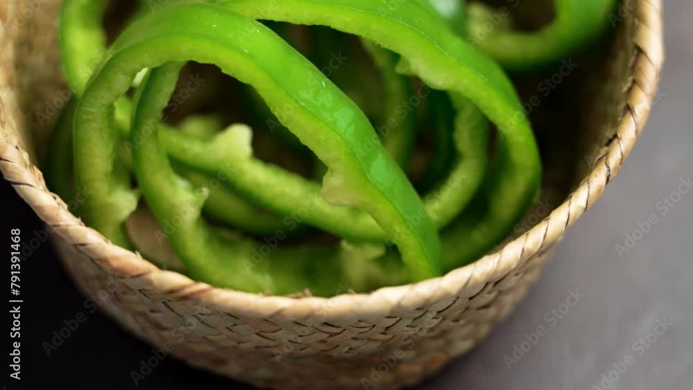Fresh sliced green bell peppers in a wicker kitchen bowl on a wooden table closeup. Vegetable source of vitamin C. Rotation Fresh sliced green bell peppers in a wicker kitchen bowl on a wooden table closeup. Vegetable source of vitamin C. Rotation