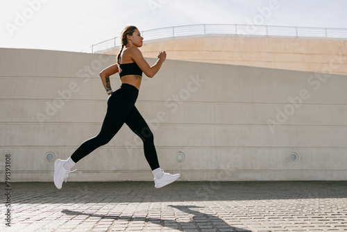 Active woman athlete is jogging in morning on modern building background. Healthy life concept