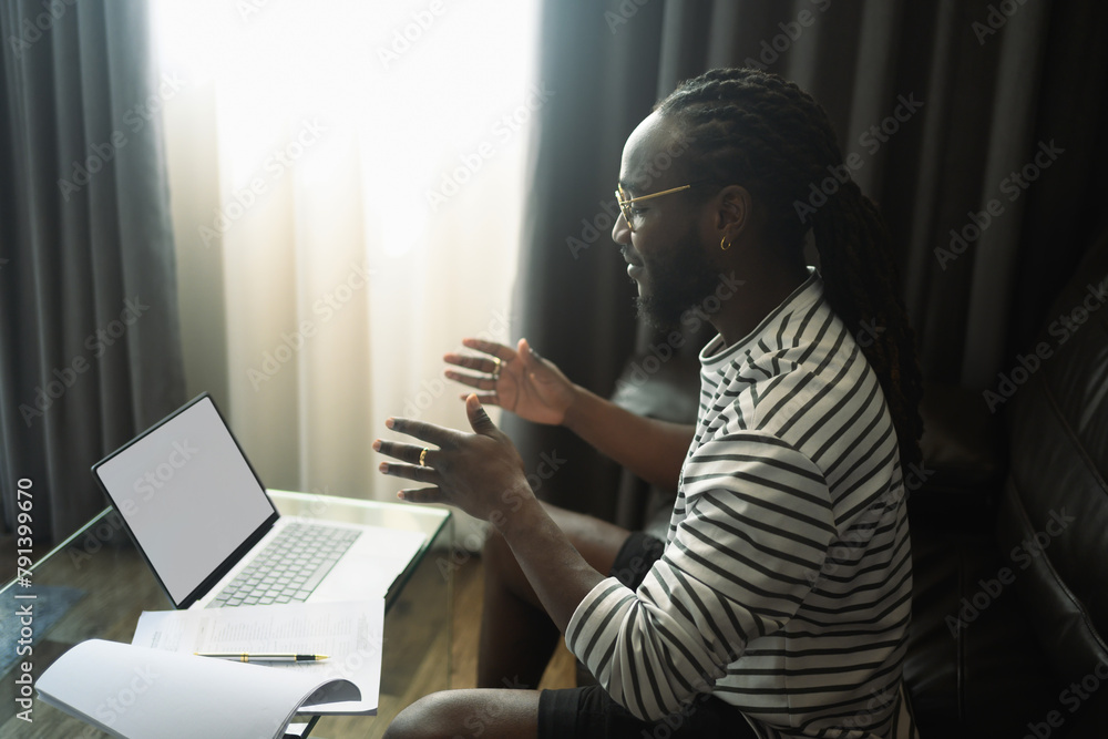 Side view of young African man talking on video call on laptop at home Side view of young African man talking on video call on laptop at home