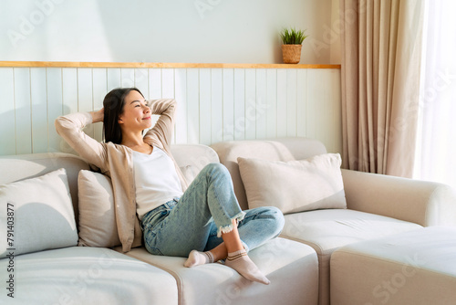 Carefree Asian woman relaxing and sitting on a sofa at home in the morning