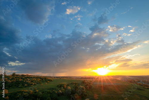 Optimistic summer scenery. The majestic sunset scene with approaching rainy clouds with falling rain over green summer hills. Beautiful sunset sky with clouds and sunshine. Summer nature background.