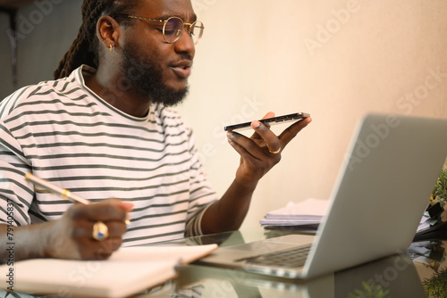 African American man having phone conversation and working with laptop on kitchen table