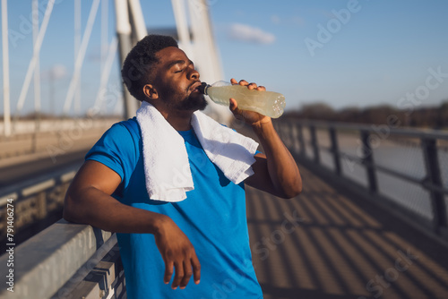 Portrait of young african-american man who is drinking water and relaxing after jogging.