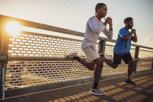 Two african-american friends are exercising on the bridge in the city. They are doing squats.