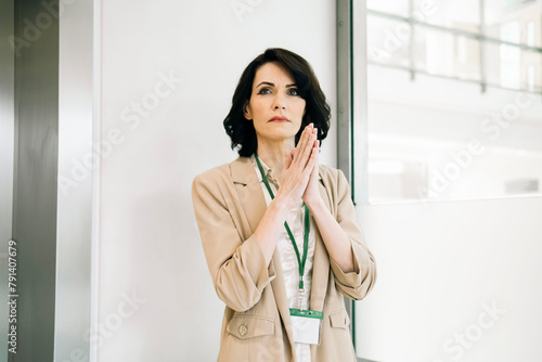 Worried mature businesswoman standing with hands clasped at office photo