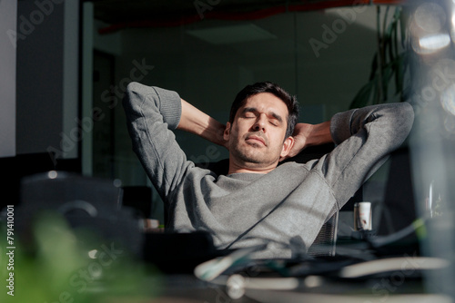 Tired businessman relaxing with hands behind head in office photo