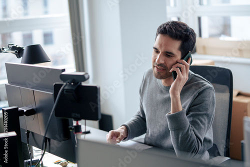 Mature businessman talking on smart phone near desktop PC at desk photo
