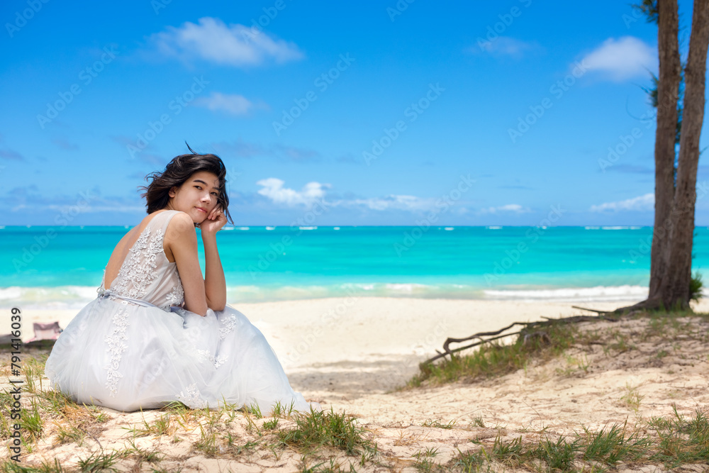 Young woman in white dress sitting on beach by ocean Young woman in white dress sitting on beach by ocean