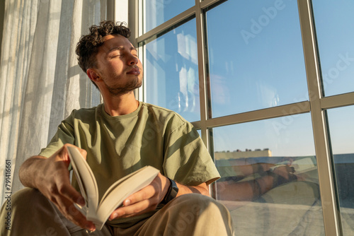 Young man sitting with eyes closed and holding book photo