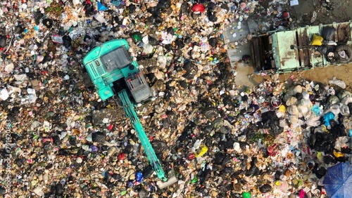 Fotografie A bird's eye view captures the vastness of waste management, with a teal excavator and dump truck amid scattered refuse