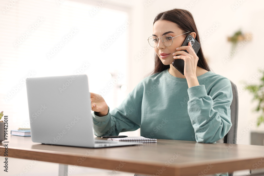 Young woman talking on smartphone during webinar at table in room Young woman talking on smartphone during webinar at table in room