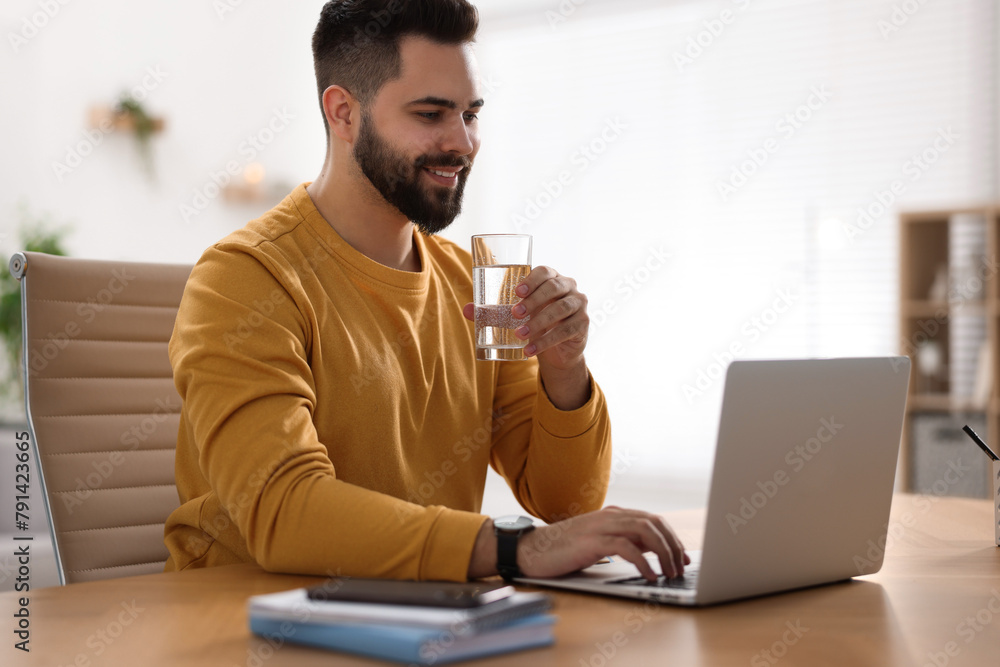 Young man with glass of water watching webinar at table in room Young man with glass of water watching webinar at table in room