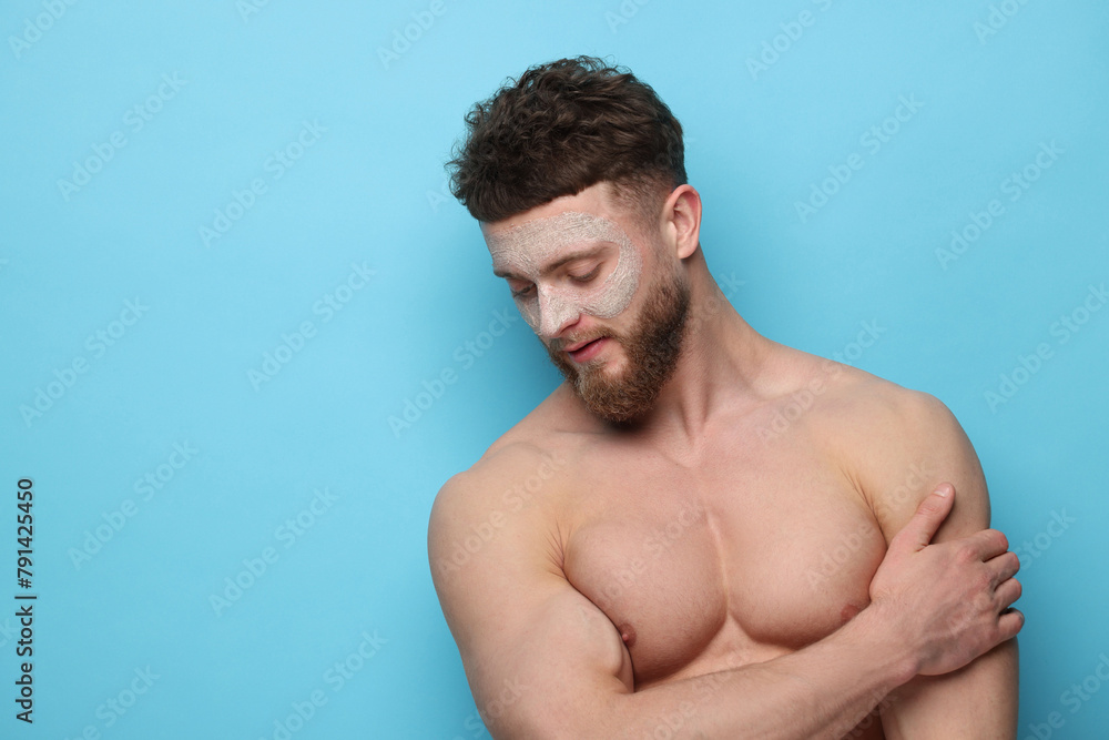 Handsome man with facial mask on his face against light blue background, space for text