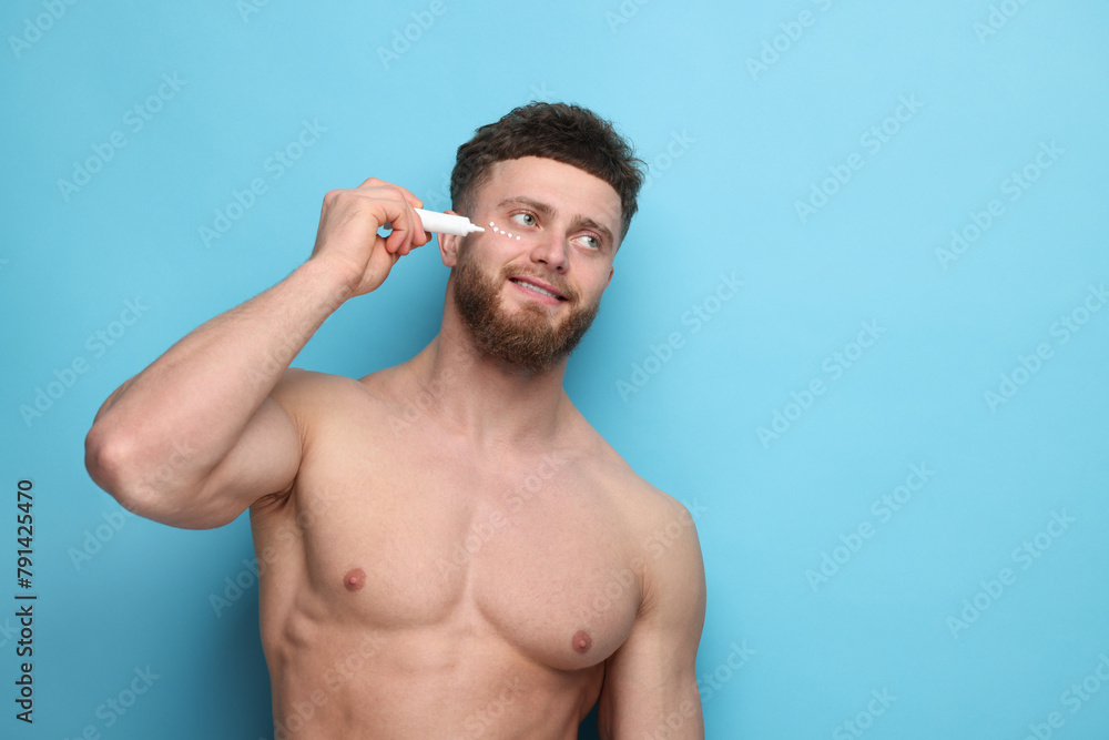 Handsome man applying moisturizing cream onto his face on light blue background, space for text Handsome man applying moisturizing cream onto his face on light blue background, space for text