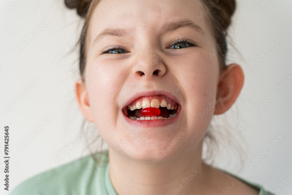Little cheerful girl holding a red pill in her teeth. Selected Focus Little cheerful girl holding a red pill in her teeth. Selected Focus