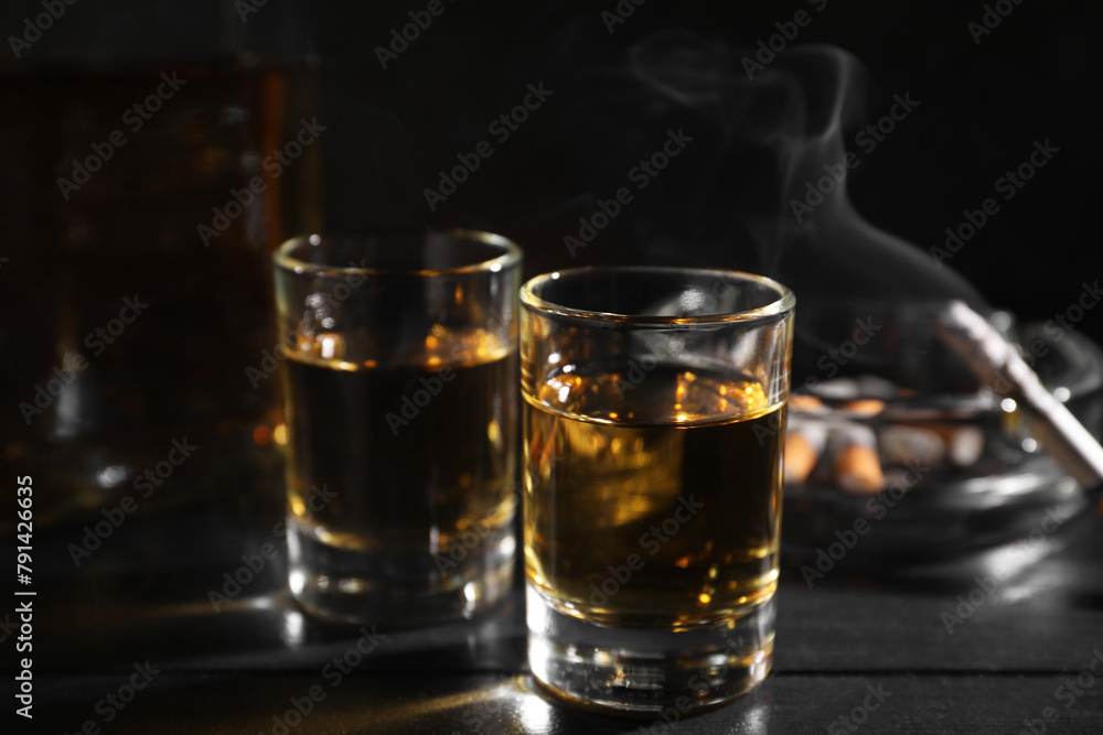 Alcohol addiction. Whiskey in glasses, smoldering cigarette and ashtray on black wooden table, closeup Alcohol addiction. Whiskey in glasses, smoldering cigarette and ashtray on black wooden table, closeup