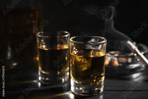 Alcohol addiction. Whiskey in glasses, smoldering cigarette and ashtray on black wooden table, closeup