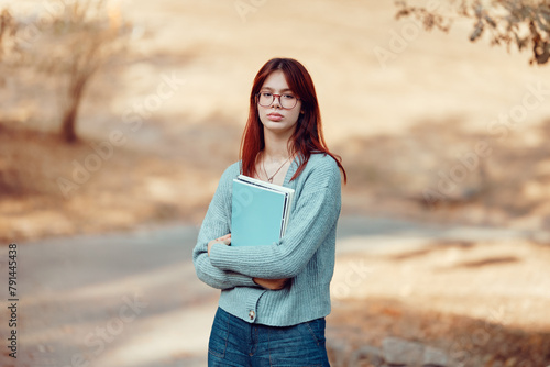Serious girl student in glasses stands holding notebooks. Hard study, student life.
