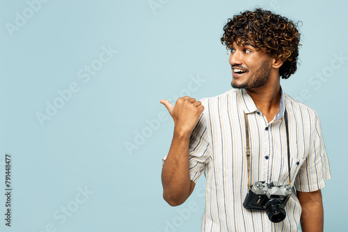 Traveler Indian man wear white casual clothes point thumb finger aside on area isolated on plain blue background. Tourist travel abroad in free spare time rest getaway Air flight trip journey concept #791448477
