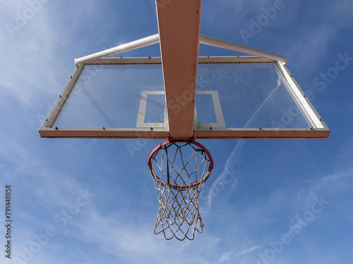 Basketball hoop with net on an outdoor court with sky background from below