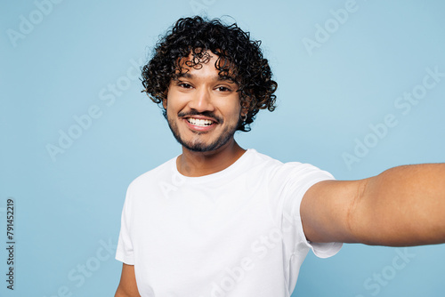 Canvas Print Close up young happy Indian man he wear white t-shirt casual clothes doing selfie shot pov on mobile cell phone isolated on plain pastel light blue cyan background studio portrait