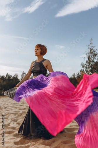 Full length of woman in belly dancing costume waving with fan veils and dancing in nature 