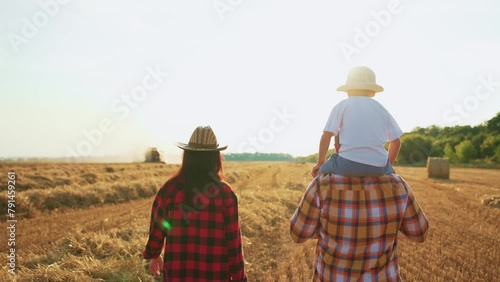 Family walk man son mom on nature at sunset. Father holding boy on shoulders walking on field with haystacks. Child with flying arms playing with dad. People enjoying nature, active recreation. photo