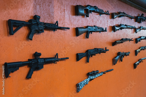 Firearms, rifles and shotguns on an orange wall in a shooting range.