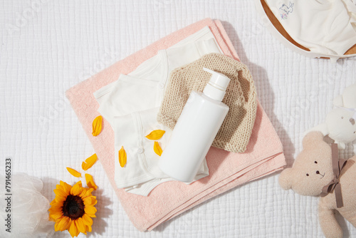 Daily baby care products for skin care or bathing with unlabeled bottle on pink bath towel, decorated by a sunflower and a brown bear. Blank space for adding designing elements, high angle shot
